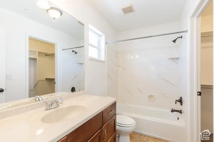 Bathroom featuring a vanity with a light-toned countertop, large wall-mounted mirror, wood-finish cabinetry, shower-tub combination with patterned wall tile, and bronze-finish plumbing fixtures