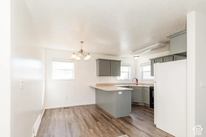 Kitchen featuring grey cabinetry, wood-finish flooring, a peninsula breakfast bar, and a multi-arm chandelier