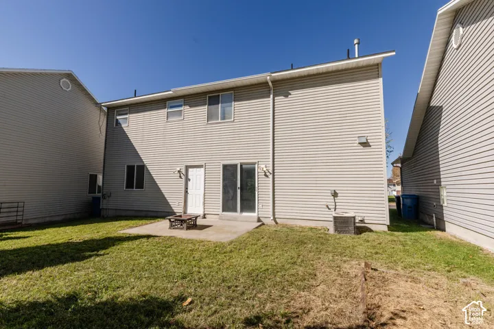 Rear exterior featuring light-toned vinyl siding, a concrete patio, and a grass lawn
