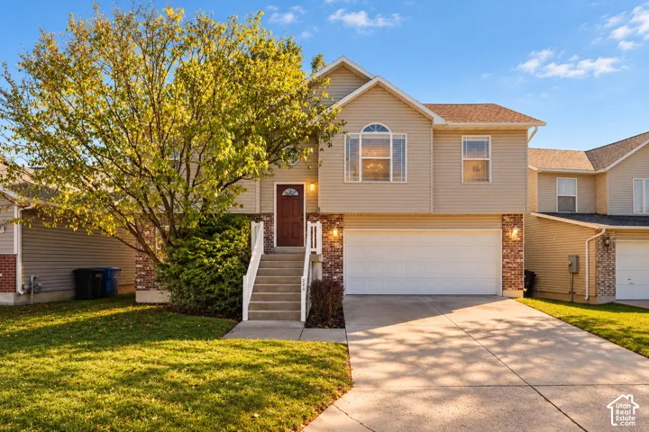 Two-story exterior featuring light-toned horizontal siding, brick masonry accents, an attached two-car garage, concrete driveway, and an elevated entry staircase with white railings