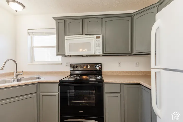 Kitchen featuring grey cabinetry, solid-surface countertops, black electric range, white over-the-range microwave, and stainless steel pull-down faucet