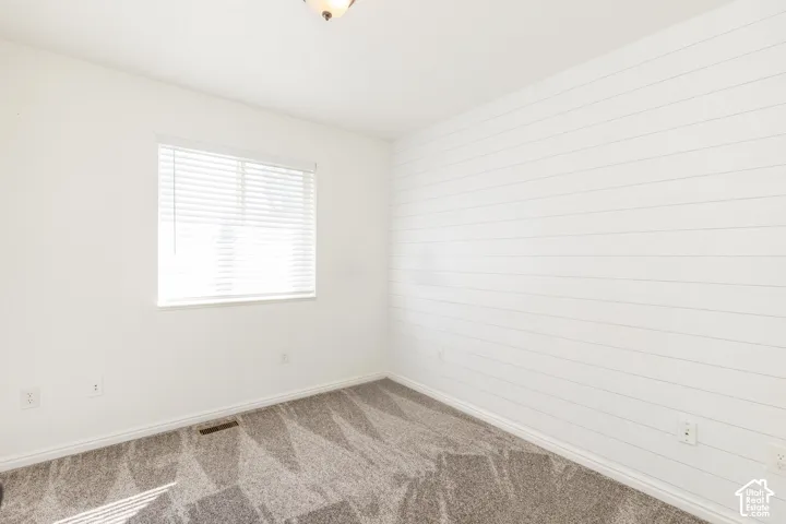 Room featuring horizontal white plank accent wall, neutral carpeting, and a window with white horizontal blinds