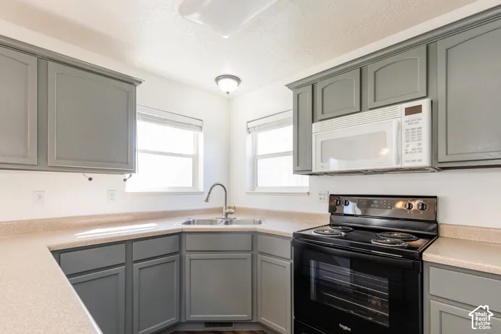 Kitchen featuring grey cabinetry, solid-surface countertops, dual-basin sink with a gooseneck faucet, black electric range, and an over-the-range microwave
