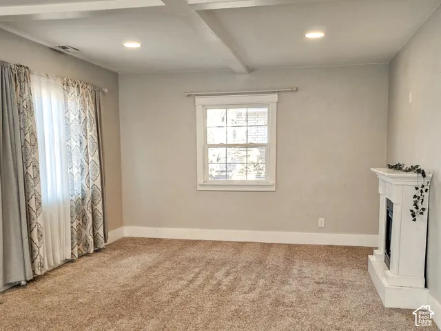 Living area featuring a ceiling with decorative beams, recessed lighting, carpeted flooring, a multi-pane window with substantial trim, and a white fireplace surround