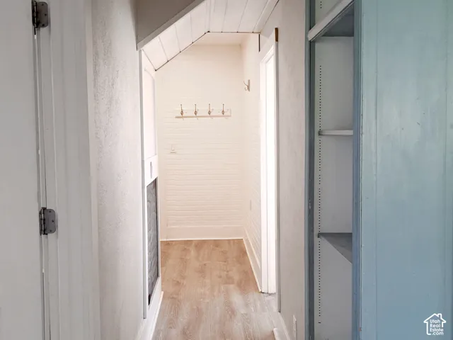 Hallway featuring wood-finish flooring, white brick-pattern wall accents, built-in shelving, tongue-and-groove ceiling paneling, and wall-mounted metal hooks