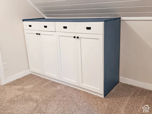Built-in cabinetry featuring white shaker-style doors, four drawers with matte black hardware, and a solid blue countertop, positioned beneath a sloped ceiling with horizontal planking