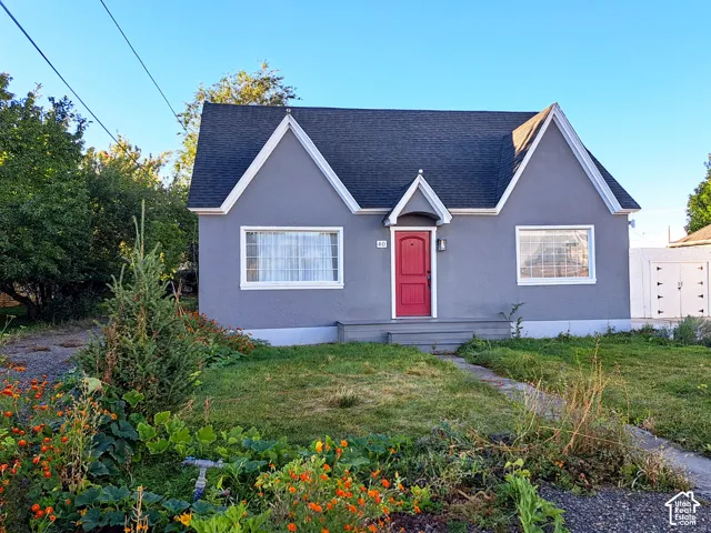 Exterior facade featuring a steep-pitched roofline with dual gables, stucco siding, a front entryway with a decorative hood, and a solid red front door