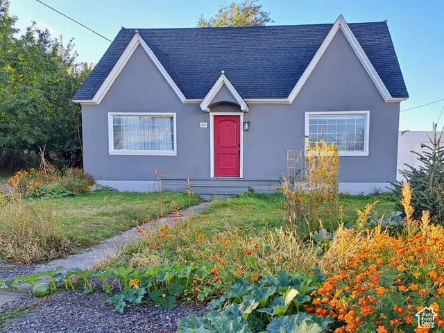 Cottage-style exterior featuring a dual-gable roofline, stucco siding, and a central entry door with a decorative hood