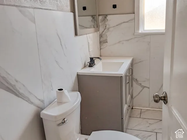 Vanity featuring a rectangular basin, stone-composite countertop, and dark-finish hardware, complemented by large-format veined wall tile and matching floor tile