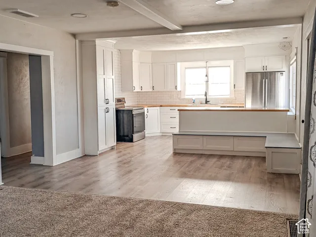 Kitchen featuring white cabinetry, wood-finish flooring, built-in breakfast nook seating, stainless steel appliances, and a light-toned countertop