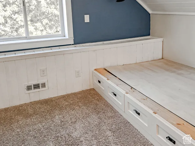 Built-in platform storage with white cabinetry, beadboard wall paneling, sloped ceiling, and textured carpeting