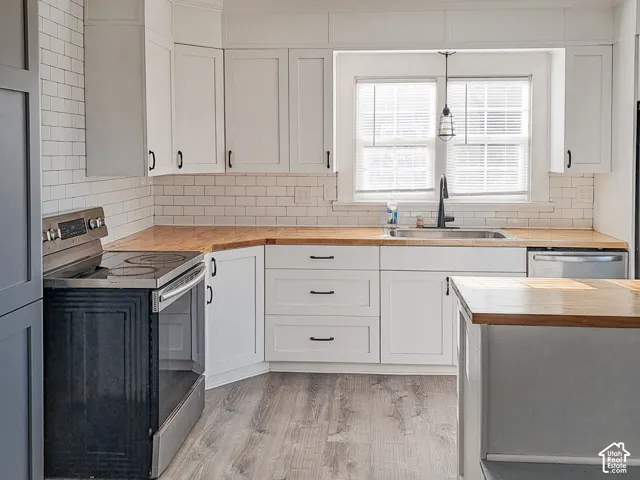 Kitchen featuring white cabinetry, wood-finish countertops, subway tile backsplash, matte black hardware, and wood-finish flooring