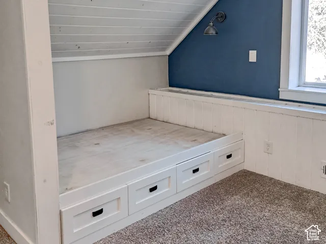 Built-in platform featuring integrated storage drawers with matte black hardware, white tongue-and-groove paneled walls, slanted ceiling detail, and wall-mounted industrial-style sconce