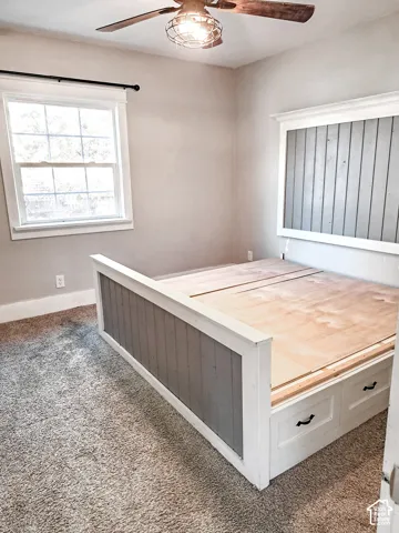 Built-in platform frame featuring integrated storage drawers and vertical wood-plank detailing, overhead industrial-style cage light fixture, multi-pane window with trim surround, and neutral wall tones