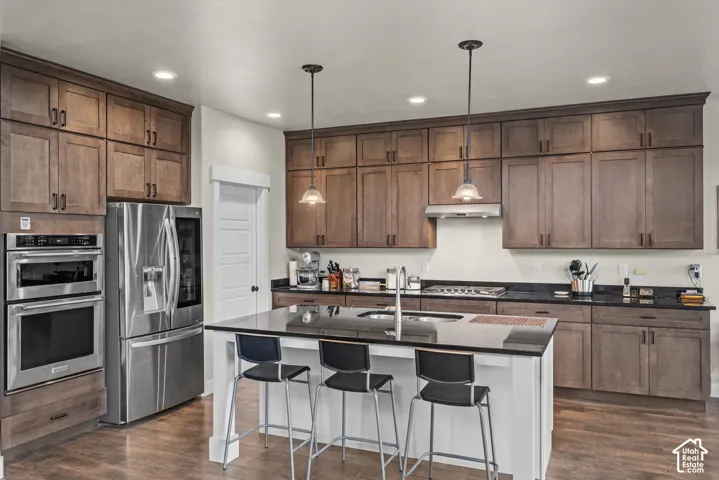 Kitchen featuring stained wood cabinetry, stone countertops, central island, stainless steel built-in double ovens, and stainless steel refrigerator