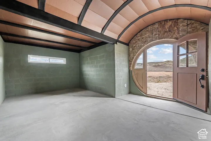 Interior space featuring a vaulted barrel ceiling with exposed structural steel beams, concrete block walls, a concrete floor, and a circular entry door