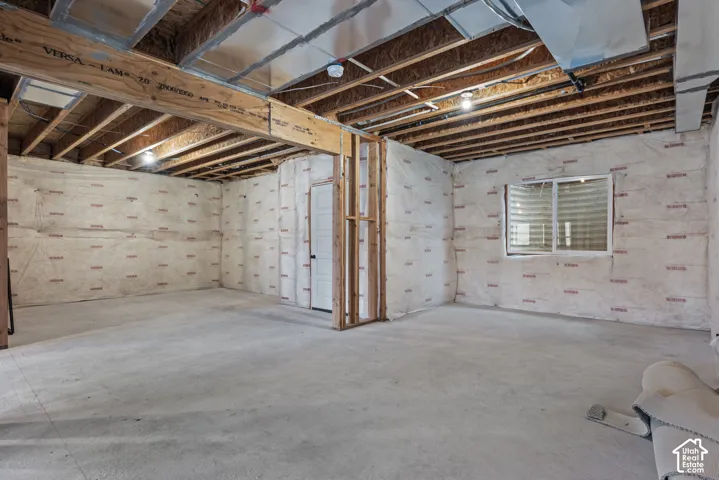 Unfinished basement featuring exposed wood joists, a structural support beam, concrete flooring, insulated walls, and a single-pane window
