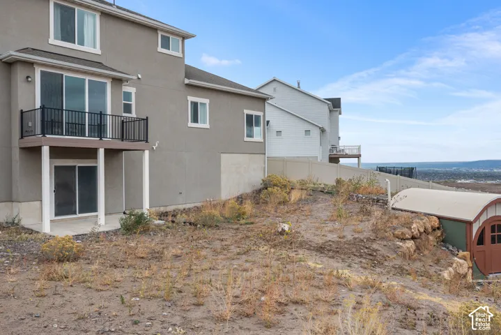 Stucco exterior featuring an elevated deck with black metal railing, concrete lower patio, and a detached arched storage structure