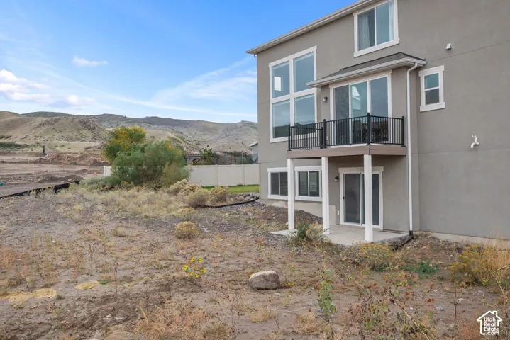 Multi-story stucco exterior featuring a raised balcony with black metal railing, sliding glass doors, double-height windows, and a ground-level concrete patio