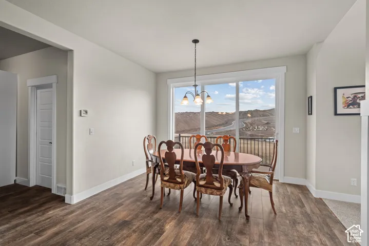 Wood-finish flooring, three-light metal chandelier, and large sliding glass door with a hillside landscape backdrop