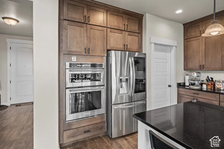 Kitchen featuring stained wood cabinetry, stainless steel double wall ovens, stainless steel French door refrigerator, dark stone countertops, and wood-finish flooring