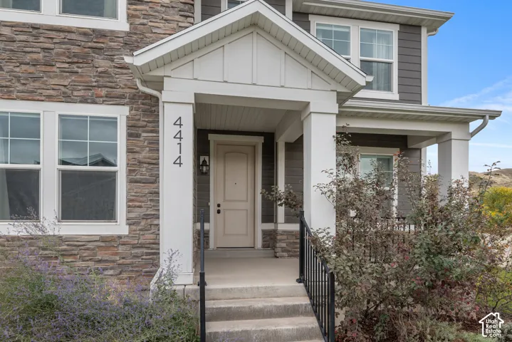 Exterior facade featuring stacked stone veneer, horizontal siding, a covered entryway with white columns, and a metal handrail