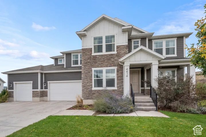 Multi-story exterior featuring stone veneer siding, horizontal lap siding, vertical board-and-batten gables, a covered entryway with structural columns, and a three-car garage