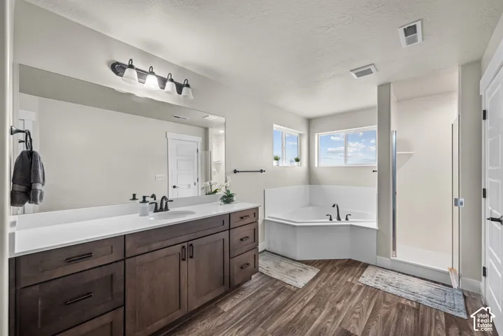 Bathroom featuring a vanity with dark wood-finish cabinetry, a white countertop with an integrated sink, a corner soaking tub, a separate glass-enclosed shower, and wood-finish flooring