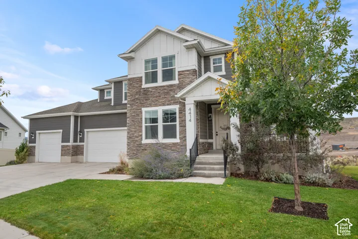 Two-story exterior featuring stone veneer siding, board and batten gables, a covered front porch with iron railings, and a three-car garage