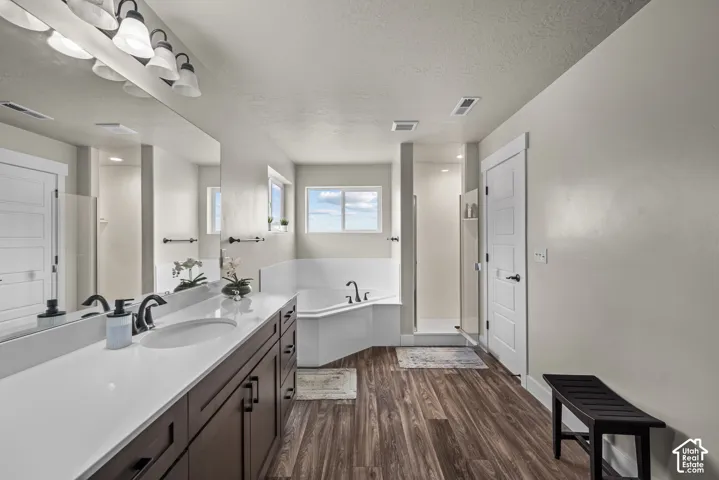 Dark wood-finish vanity with a white countertop, undermount sink, multi-light fixture, corner soaking tub, and wood-finish flooring