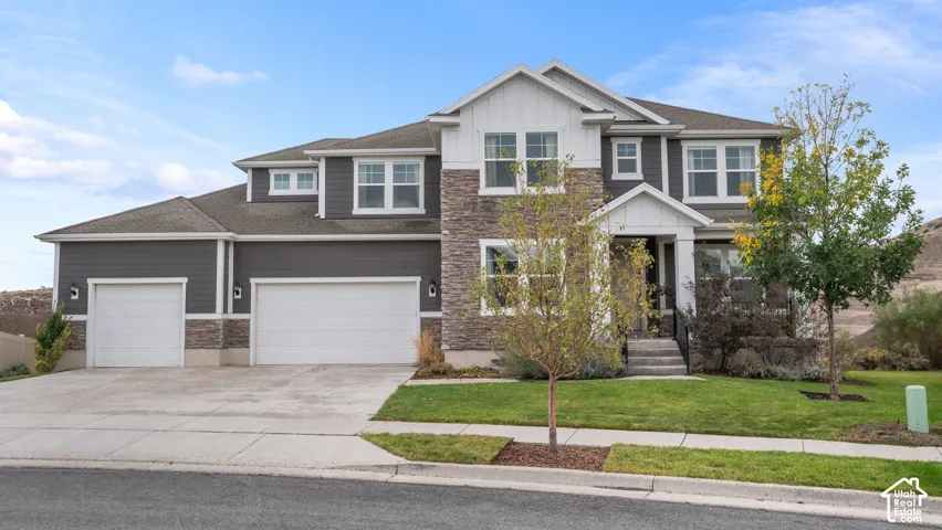 Two-story exterior featuring stone veneer siding, horizontal lap siding, a three-car garage, and a covered front porch entry