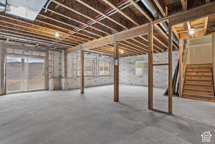 Unfinished lower level featuring exposed joist ceilings, concrete flooring, sliding glass door, and wooden staircase