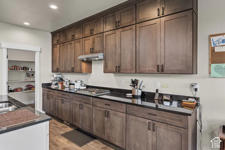 Custom cabinetry with extended upper storage, dark stone countertops, stainless steel gas cooktop, integrated range hood, and walk-in pantry