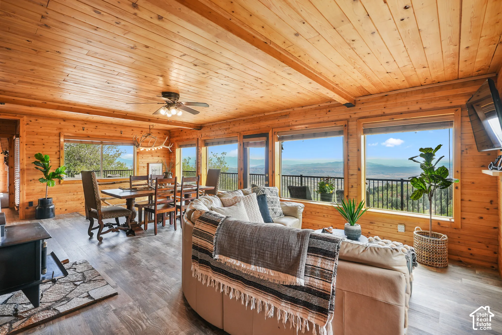 Interior featuring natural wood-plank walls and ceiling, large picture windows, a stone-surround wood-burning stove, and a railed outdoor deck