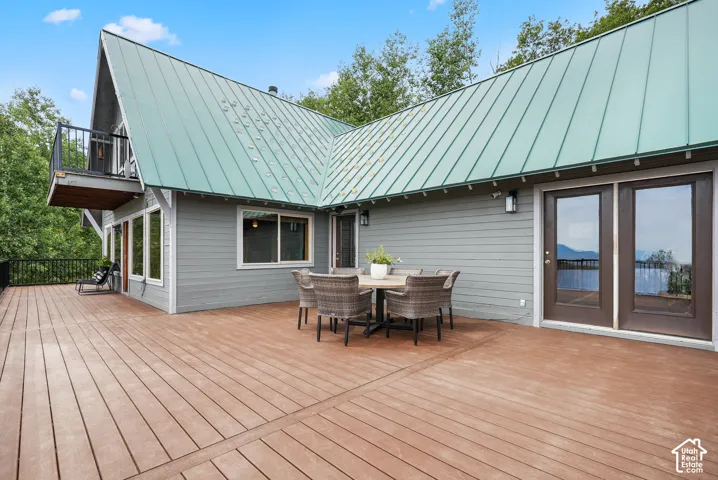 Expansive wood-finish deck with metal railing, green standing-seam metal roof, horizontal siding, and double glass-panel doors