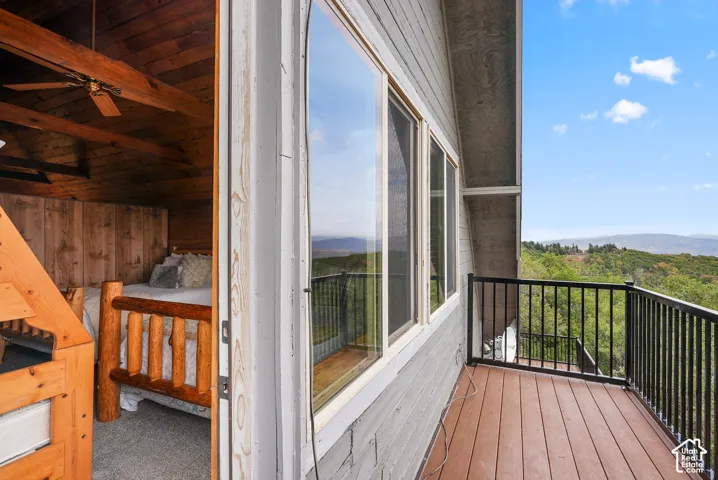 Exterior balcony featuring composite decking and a black metal railing, with interior exposure showcasing natural wood-plank ceilings and exposed wooden structural beams