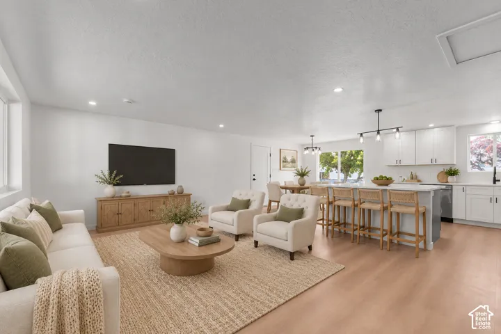 Open-concept living space featuring wood-finish flooring, recessed lighting, white shaker-style cabinetry, and a large kitchen island with pendant lighting