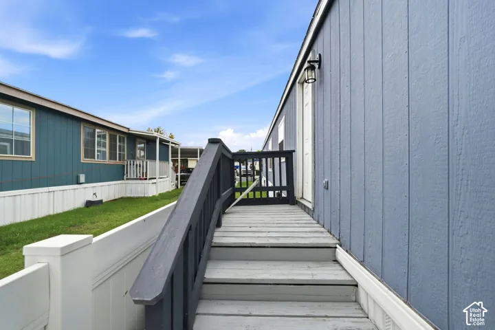Exterior entrance featuring vertical siding, wooden staircase, metal railing, and wall-mounted outdoor lighting