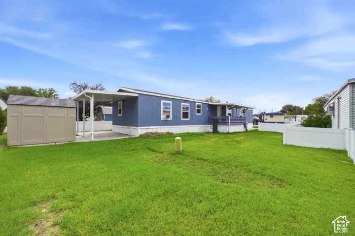 Exterior featuring blue siding, a covered carport, a detached storage shed, a raised porch, and white vinyl perimeter fencing