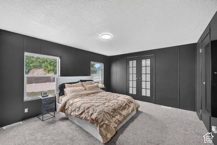 Bedroom featuring dark paneled walls, French doors with multi-lite glass panes, integrated floor-to-ceiling cabinetry, dual windows, and wall-to-wall carpeting