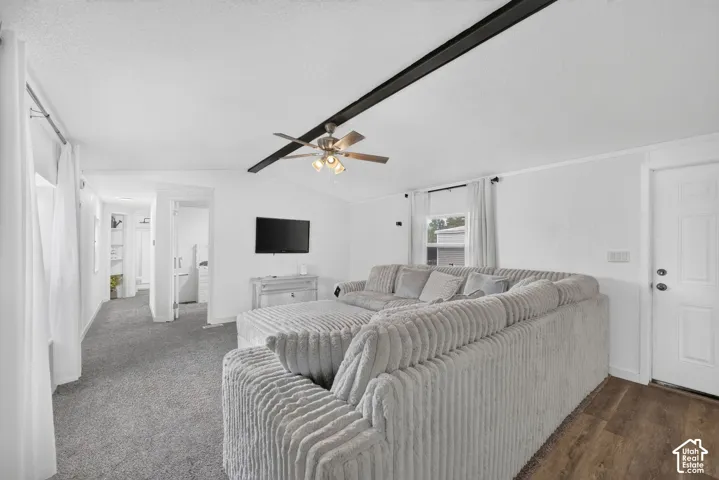 Interior space featuring a dark, exposed structural ceiling beam, a ceiling-mounted light fixture with a fan, wall-to-wall carpeting, wood-finish flooring at the entryway, and a multi-panel exterior door
