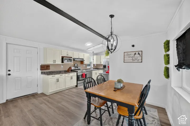 Kitchen featuring off-white cabinetry, stone-finish countertops, stainless steel appliances, wood-finish flooring, and a spherical metal pendant light fixture