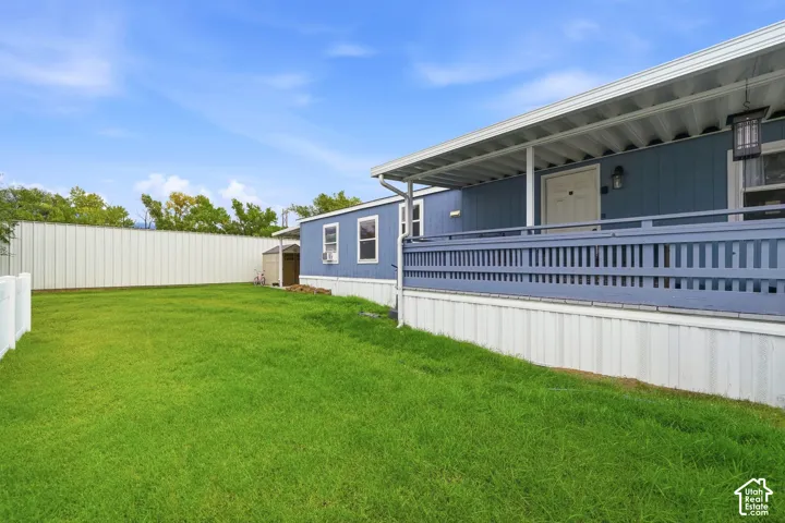 Exterior space featuring a covered porch with wooden railings, vinyl siding, a metal privacy fence, and an expansive lawn area