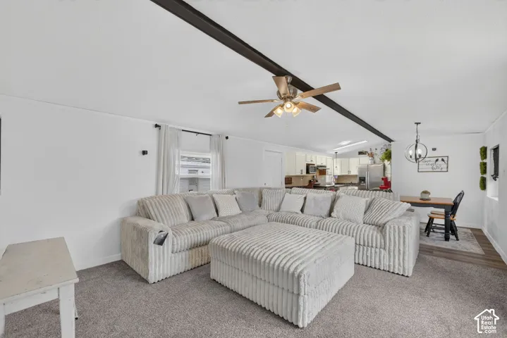 Open-concept interior featuring a decorative ceiling beam, central ceiling fan with integrated lighting, neutral carpet flooring, and a globe-style pendant light