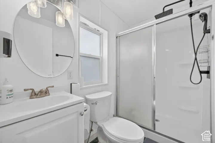 Bathroom featuring a vanity with integrated sink, circular mirror, multi-light fixture, and a shower enclosure with a rainfall shower head and sliding glass door
