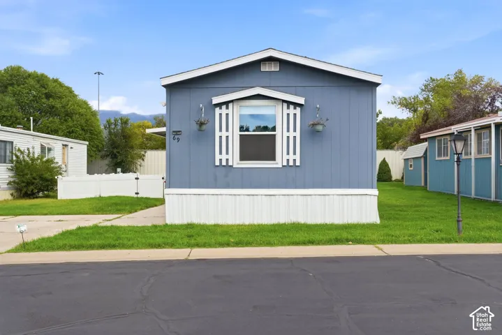 Blue exterior siding with white trim, accented by decorative window shutters, dual wall-mounted light fixtures, and a white privacy fence
