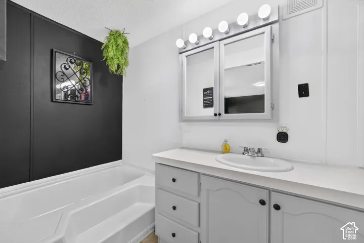 Bathroom vanity featuring painted cabinetry, an integrated oval sink, a multi-bulb light fixture, and a dual-door medicine cabinet, accompanied by a white soaking tub set against an accent wall