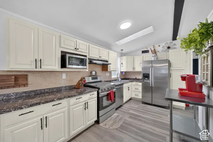 Kitchen featuring off-white cabinetry, dark stone-finish countertops, stainless steel appliances, a recessed skylight, and wood-finish flooring