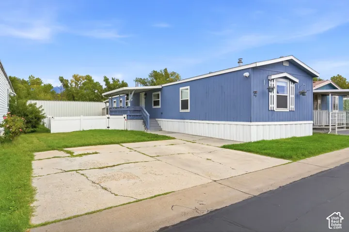 Blue exterior siding, white skirting, concrete driveway, covered porch with stairs, and enclosed white fencing