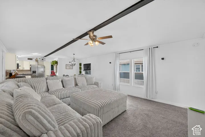 Open-concept living space featuring a central exposed structural beam, neutral wall-to-wall carpeting, and a ceiling-mounted light fixture with a fan